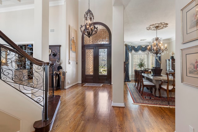 entrance foyer with ornamental molding, stairway, wood finished floors, and an inviting chandelier