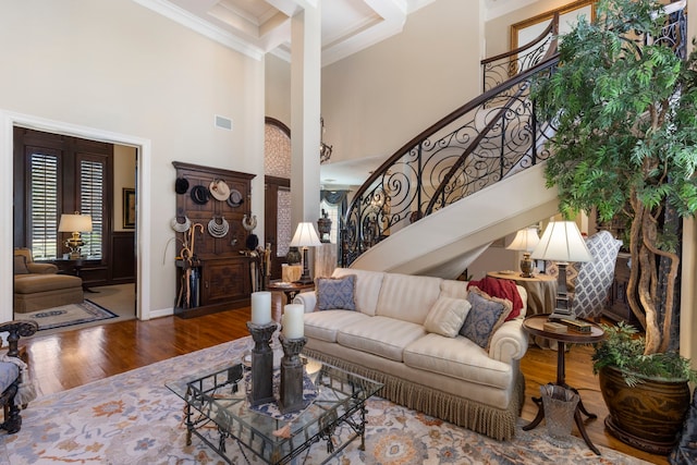 living area featuring wood finished floors, visible vents, a towering ceiling, stairway, and crown molding