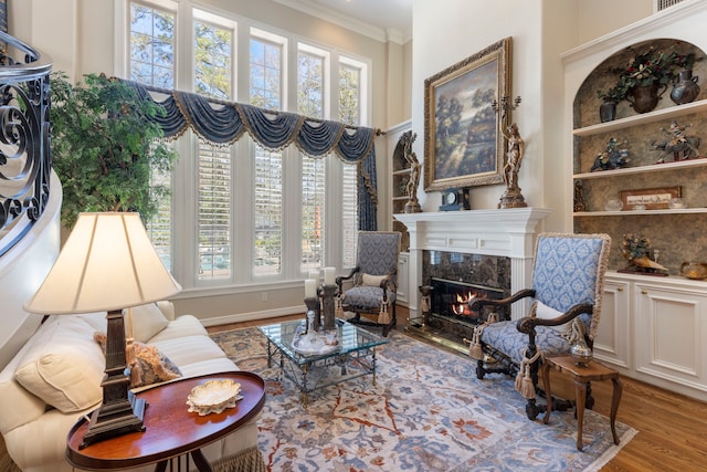 living area with built in shelves, a premium fireplace, ornamental molding, wood finished floors, and baseboards