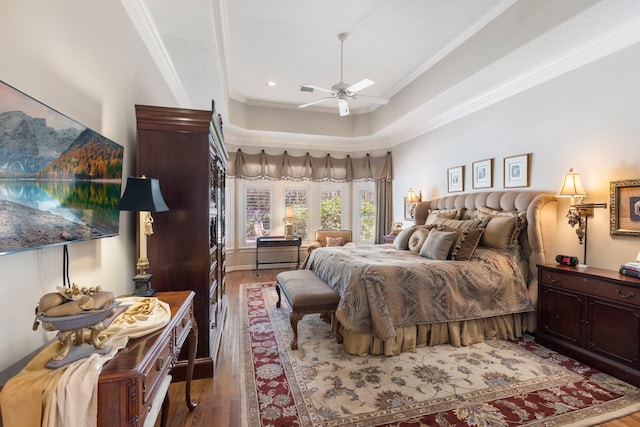 bedroom with ceiling fan, a tray ceiling, wood finished floors, and crown molding