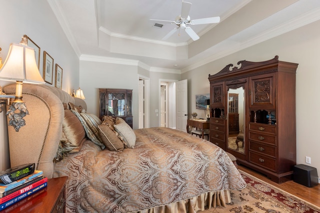 bedroom with crown molding, visible vents, a raised ceiling, and wood finished floors