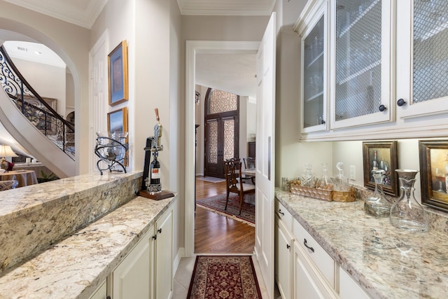 bar featuring dark wood-style floors, arched walkways, crown molding, stairway, and a bar