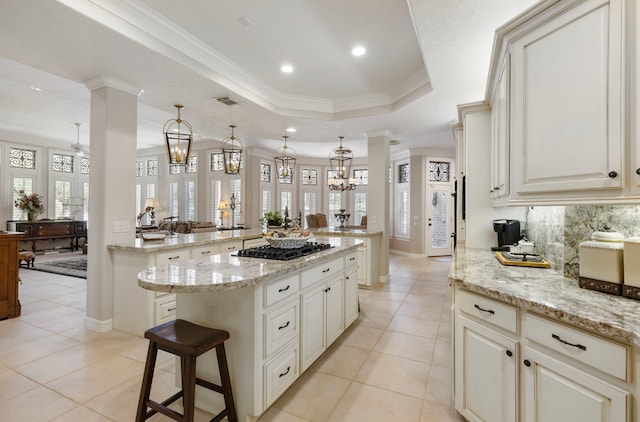 kitchen with a raised ceiling, light stone counters, a center island, hanging light fixtures, and black gas stovetop