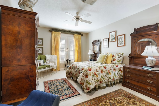 bedroom featuring light carpet, a textured ceiling, visible vents, and a ceiling fan