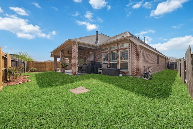 rear view of property featuring a yard, brick siding, ceiling fan, and a fenced backyard