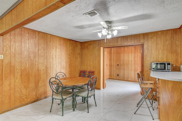 dining area with marble finish floor, visible vents, a textured ceiling, and wood walls