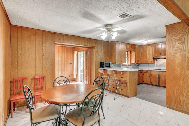 dining area with ceiling fan, a textured ceiling, wood walls, visible vents, and marble finish floor