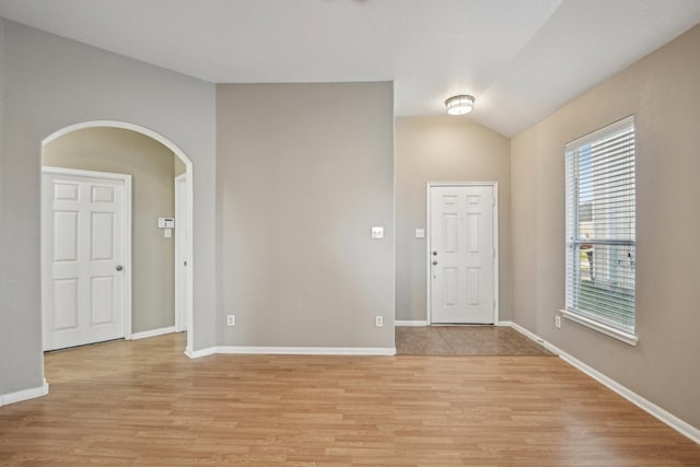 foyer featuring arched walkways, baseboards, lofted ceiling, and light wood finished floors