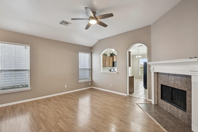 unfurnished living room with visible vents, arched walkways, ceiling fan, wood finished floors, and a fireplace