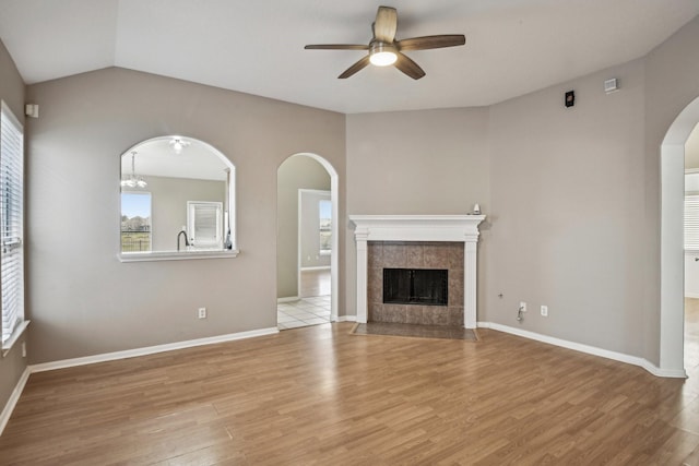 unfurnished living room with arched walkways, a fireplace, light wood-style flooring, and ceiling fan