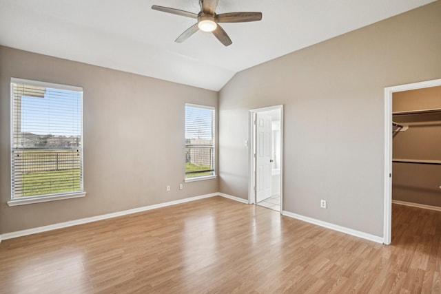 unfurnished bedroom with a closet, a spacious closet, light wood-style floors, vaulted ceiling, and baseboards