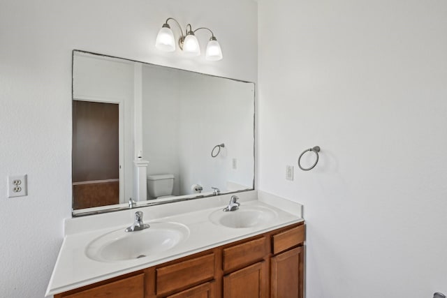 bathroom with a sink, toilet, and double vanity