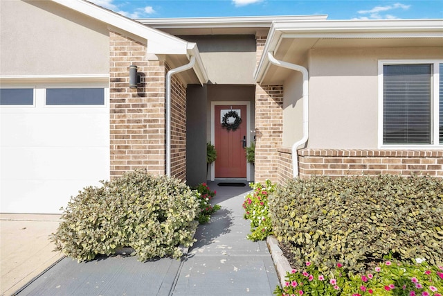 view of exterior entry with a garage, brick siding, and stucco siding