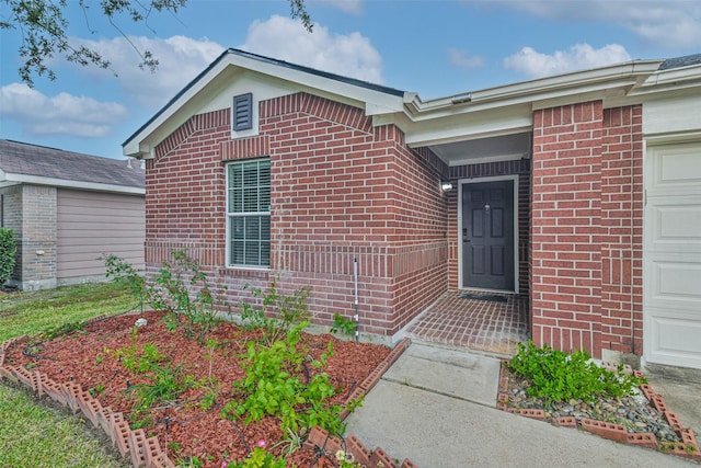 view of exterior entry featuring a garage and brick siding