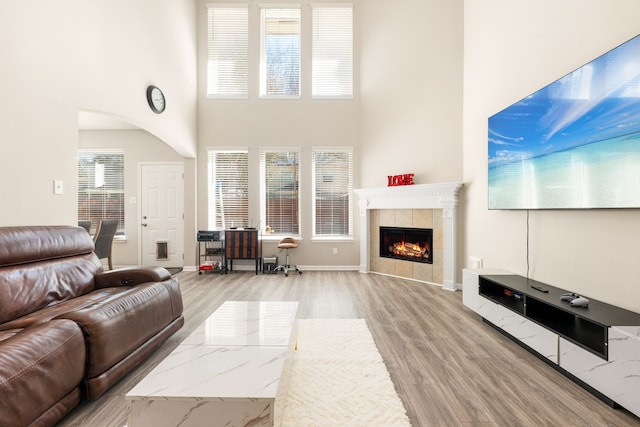 living area featuring light wood-type flooring, baseboards, a high ceiling, and a tile fireplace