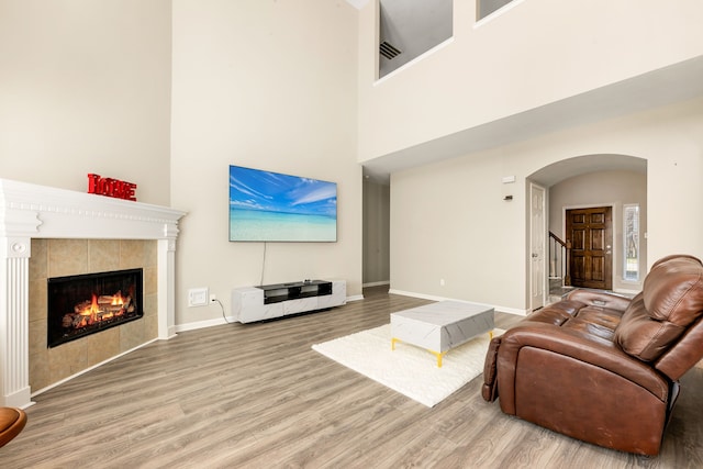 living room featuring baseboards, arched walkways, wood finished floors, stairs, and a fireplace