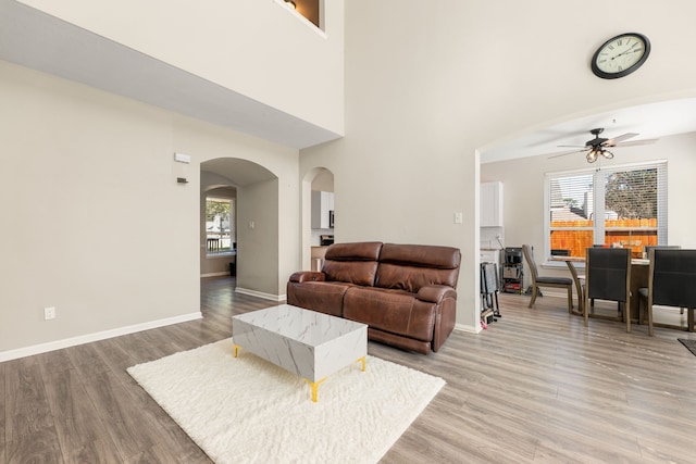 living area with arched walkways, a high ceiling, ceiling fan, wood finished floors, and baseboards