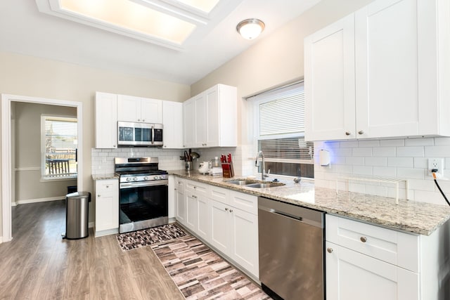 kitchen with stainless steel appliances, a sink, light stone countertops, and white cabinets