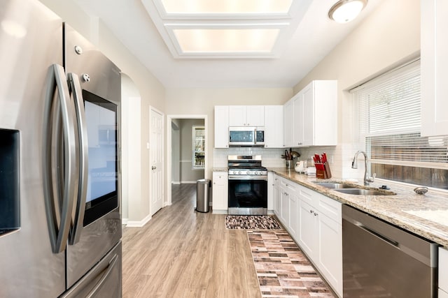 kitchen featuring light stone counters, a sink, white cabinets, appliances with stainless steel finishes, and tasteful backsplash