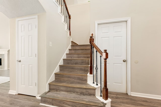 stairway with a textured ceiling, a fireplace, wood finished floors, and baseboards