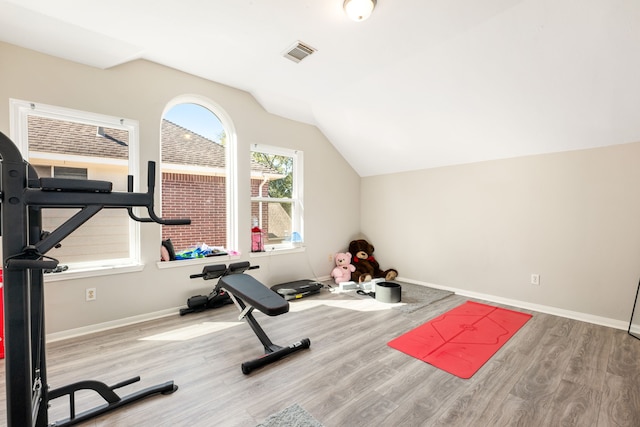 exercise room featuring light wood-type flooring, baseboards, visible vents, and lofted ceiling