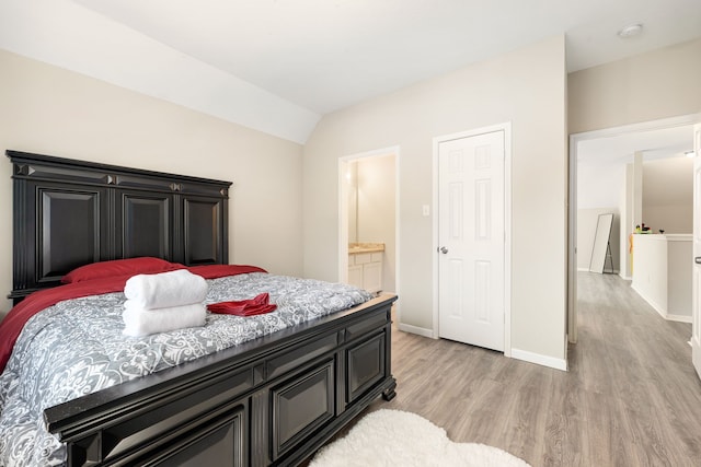 bedroom with light wood-style floors, baseboards, vaulted ceiling, and ensuite bathroom