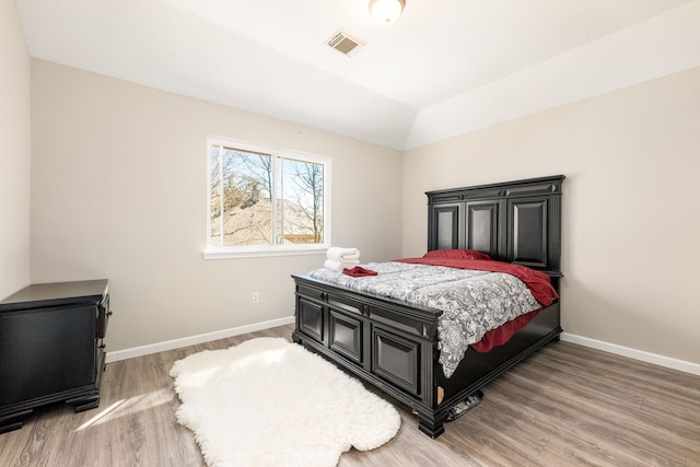 bedroom featuring vaulted ceiling, baseboards, visible vents, and light wood-style floors