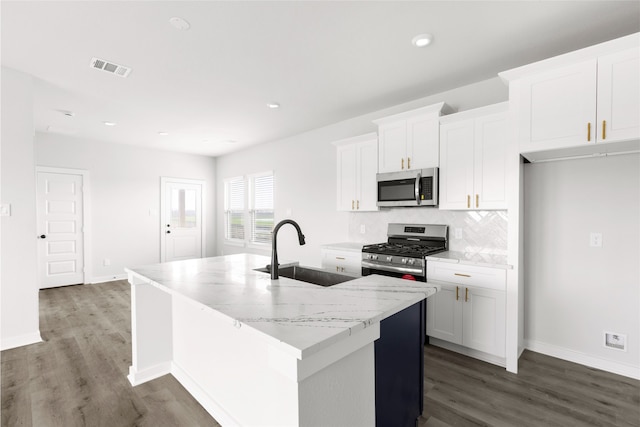 kitchen with decorative backsplash, white cabinets, an island with sink, stainless steel appliances, and a sink