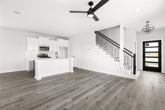 kitchen featuring a center island with sink, appliances with stainless steel finishes, open floor plan, light countertops, and white cabinetry