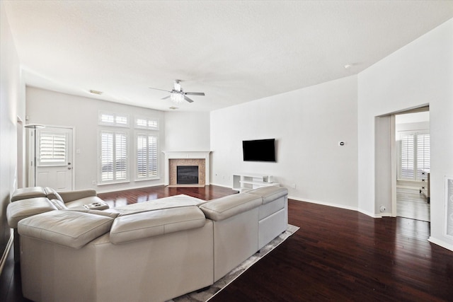 living area featuring a tiled fireplace, dark wood finished floors, a wealth of natural light, and a ceiling fan