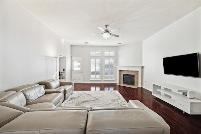 living area featuring a textured ceiling, ceiling fan, a fireplace, and dark wood-style flooring