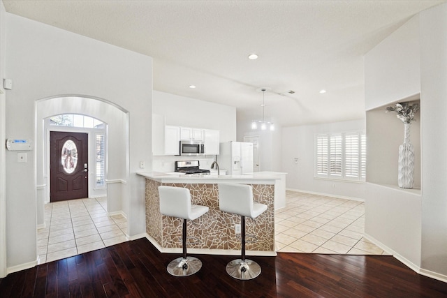 kitchen with a peninsula, white cabinetry, a kitchen breakfast bar, light countertops, and appliances with stainless steel finishes