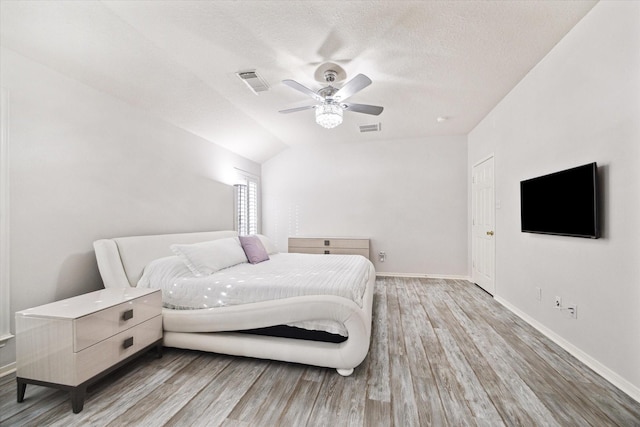 bedroom with lofted ceiling, light wood finished floors, a textured ceiling, and visible vents