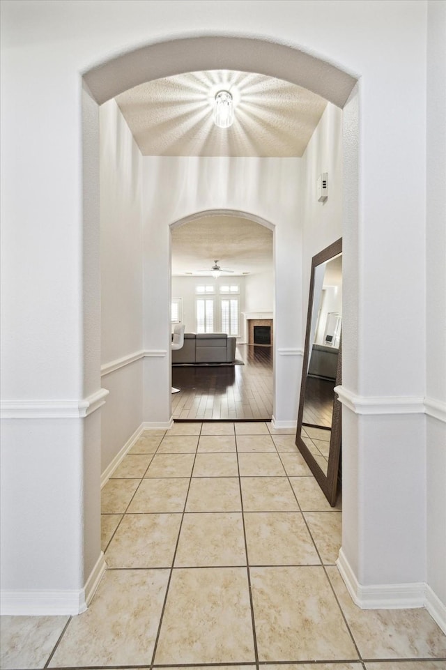 hallway featuring baseboards, arched walkways, and light tile patterned flooring