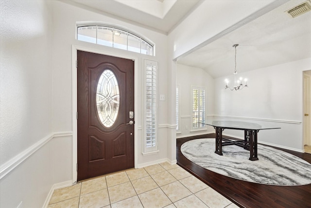 entrance foyer featuring light tile patterned floors, baseboards, visible vents, lofted ceiling, and a chandelier