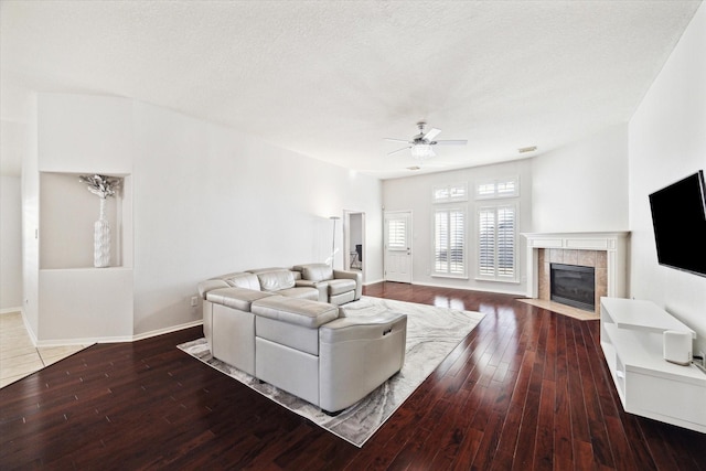 living room featuring ceiling fan, a textured ceiling, baseboards, hardwood / wood-style floors, and a tiled fireplace