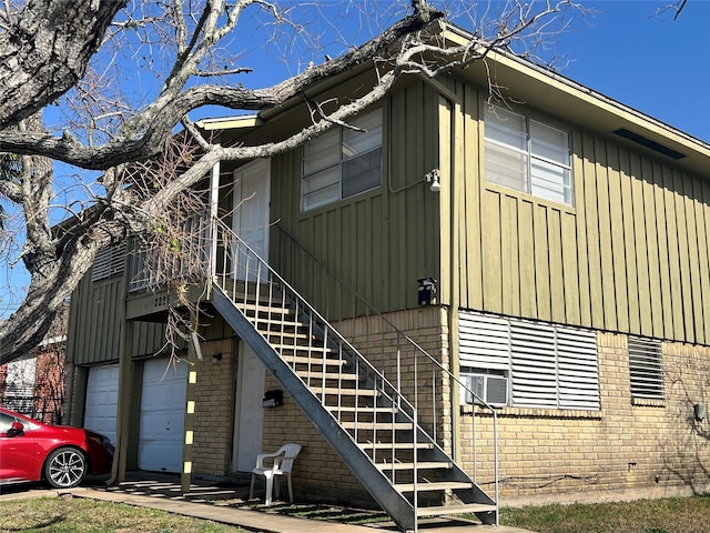 view of side of home with a garage, brick siding, and stairs