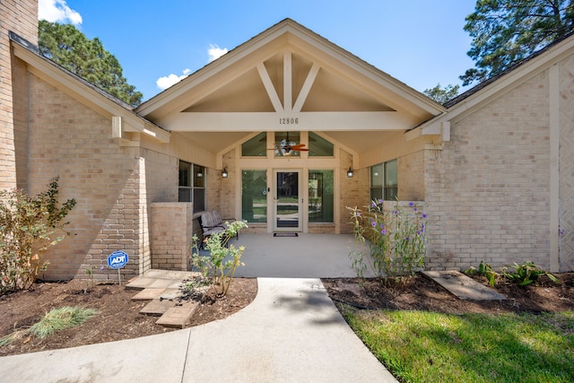 entrance to property with brick siding, a patio area, and a ceiling fan