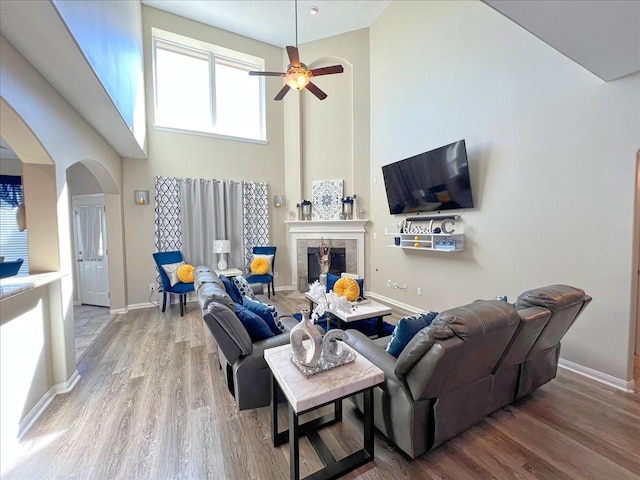 living area featuring arched walkways, wood finished floors, baseboards, and a tile fireplace