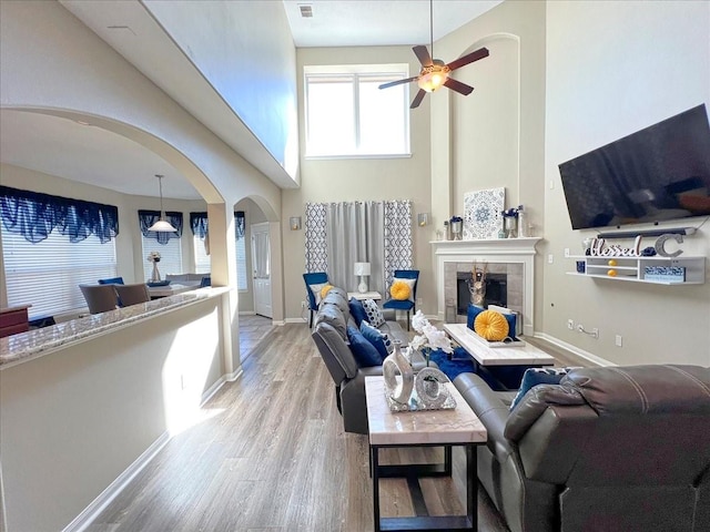 living room featuring arched walkways, ceiling fan, a fireplace, baseboards, and light wood-type flooring