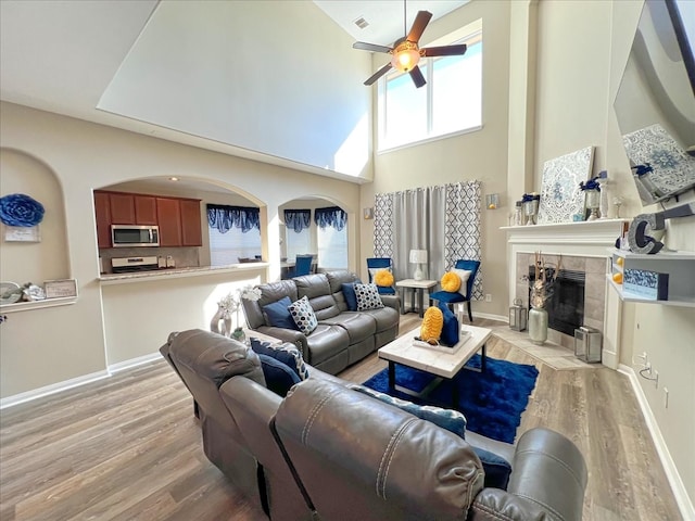 living area featuring ceiling fan, plenty of natural light, a tile fireplace, and light wood-style floors