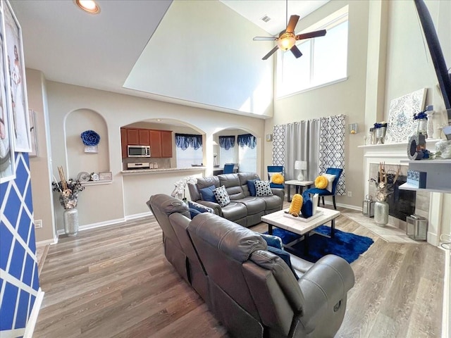 living room featuring light wood-style flooring, baseboards, ceiling fan, and a tile fireplace