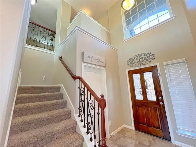 entrance foyer featuring stairs, a towering ceiling, baseboards, and light tile patterned floors