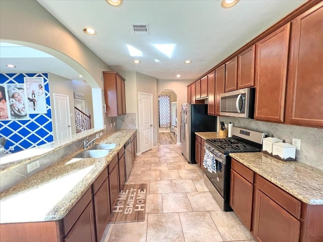 kitchen with stainless steel appliances, a peninsula, a sink, visible vents, and light stone countertops