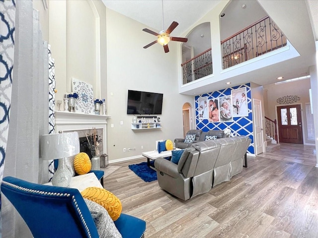 living room with arched walkways, a ceiling fan, a premium fireplace, stairway, and wood finished floors