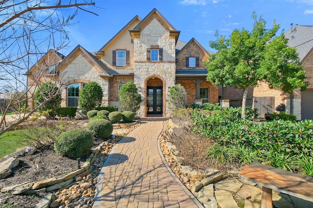 french country inspired facade with stone siding, french doors, fence, and stucco siding