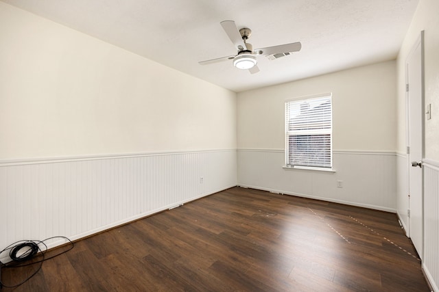 unfurnished bedroom with dark wood-style floors, wainscoting, visible vents, and a ceiling fan