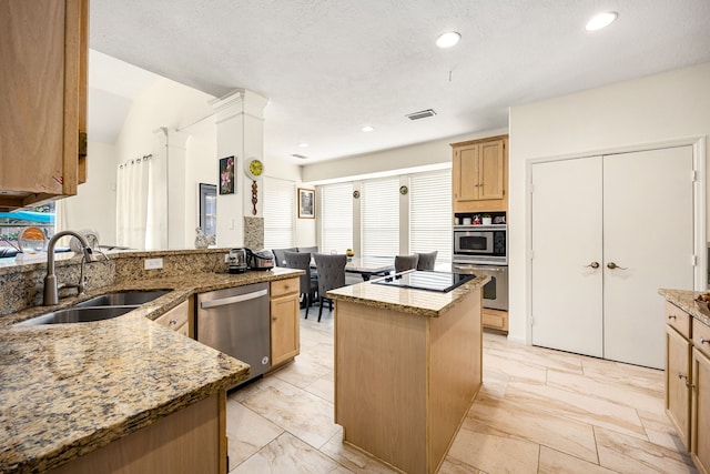 kitchen featuring light stone counters, a center island, visible vents, appliances with stainless steel finishes, and a sink