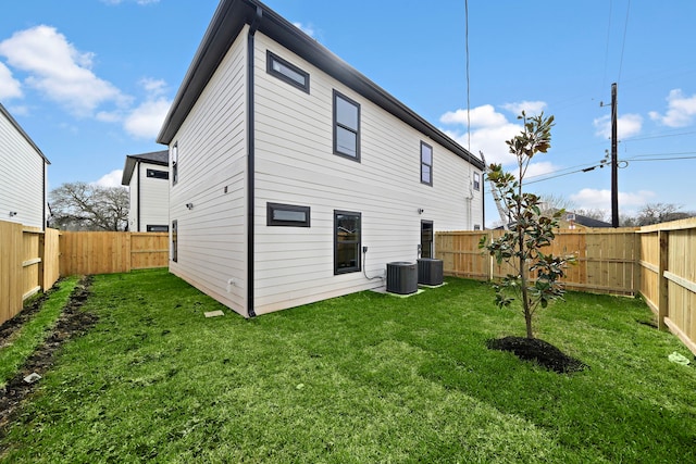 rear view of property with central air condition unit, a fenced backyard, and a yard