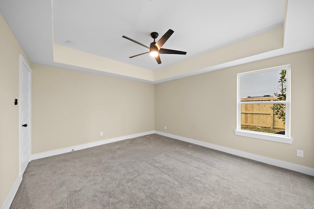 unfurnished room featuring carpet, a raised ceiling, a ceiling fan, and baseboards